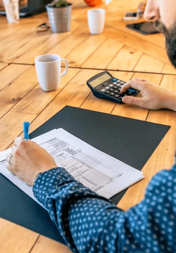 Man writing on paper with calculator at wooden table