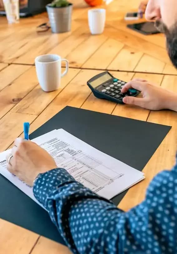 Man writing on paper with calculator at wooden table